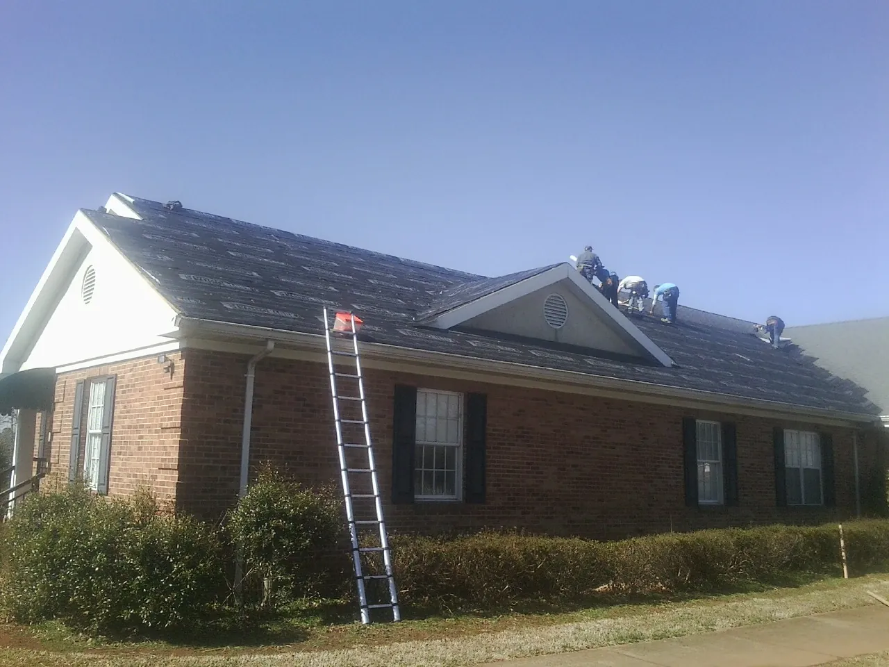 Crew tearing shingles off a brick ranch roof with a ladder set — Emergency Roof Repair work by our crew in Cherry Hill