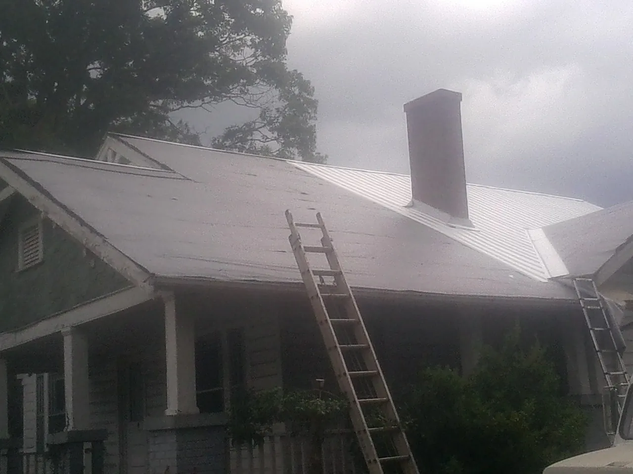 Ladders against a metal roof on an older home with a brick chimney in Cherry Hill