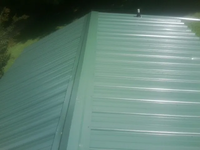 New green metal panels meeting at the ridge of a roof — Flat Roof Repair work by our crew in Cherry Hill