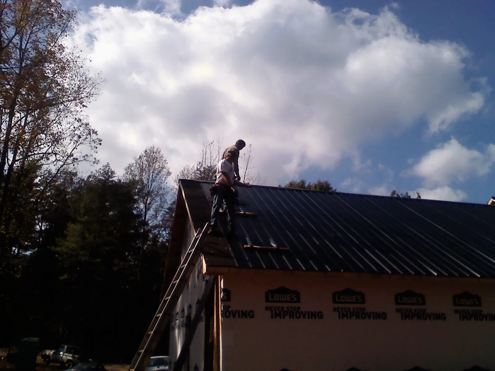 Roofer fastening dark metal panels high against a cloudy sky, from a Roof Inspection job in Cherry Hill