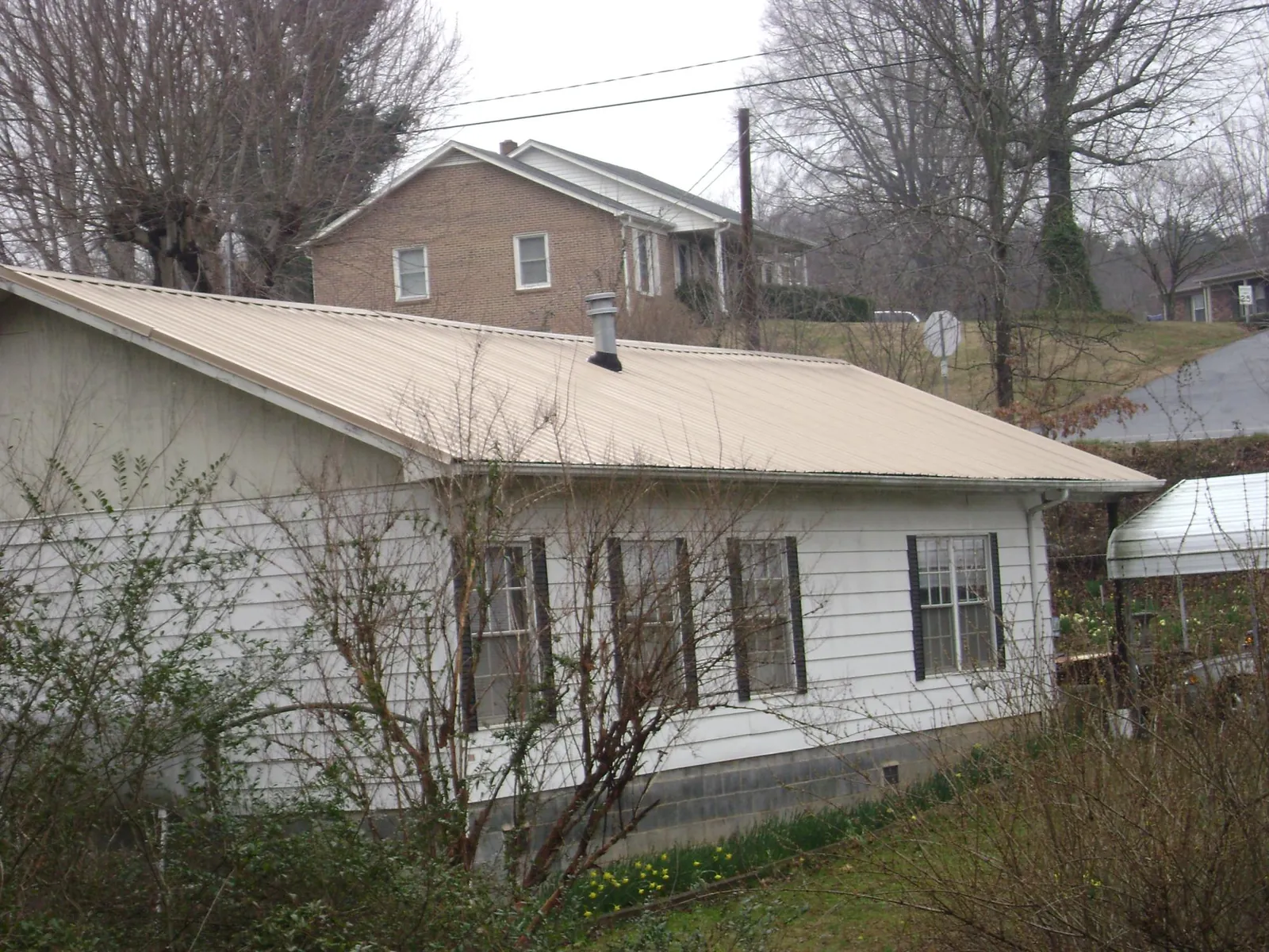 Tan metal roof on a white sided house set into a hillside — Commercial Roofing by Roofing Brothers in Cherry Hill